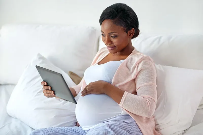 junge schwangere Frau, die Artikel auf Tablette liest