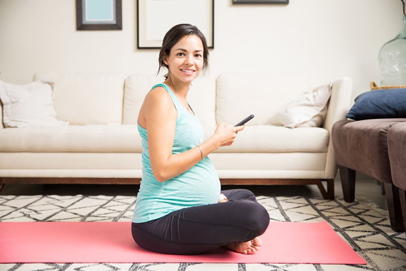 lächelnde schwangere Frau, die Telefon vor dem Training hält