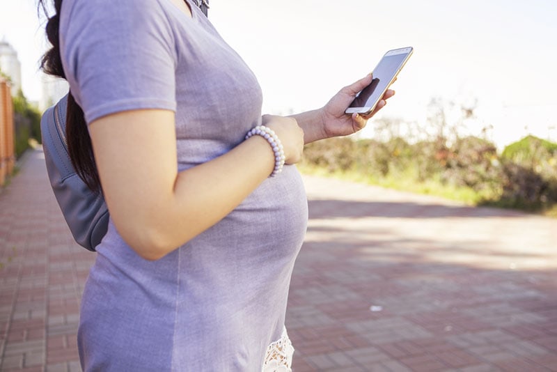 schwangere Frau, die Rucksack trägt und Telefon hält