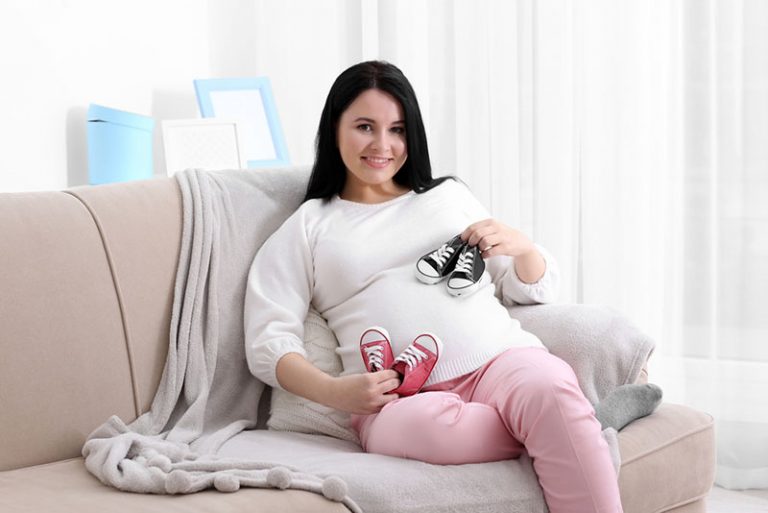 schwangere Frau, die zwei Paar Babyschuhe hält