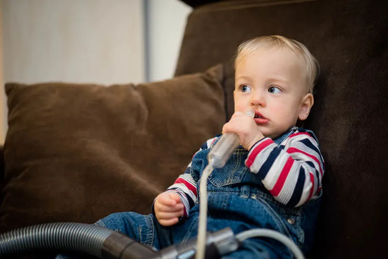 Baby hält Nasensauger mit Staubsauger verbunden