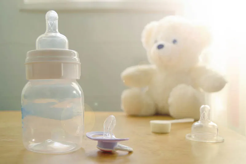 Babyflasche und Schnuller mit Spielzeug auf dem Tisch