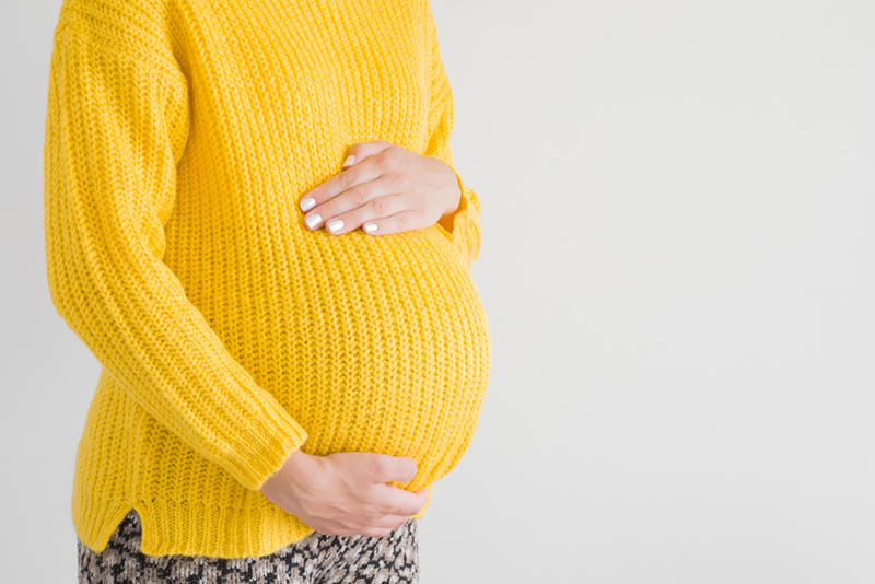 eine schwangere Frau in einem gelben Pullover