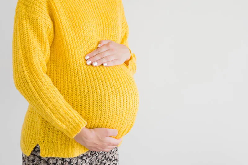 eine schwangere Frau in einem gelben Pullover
