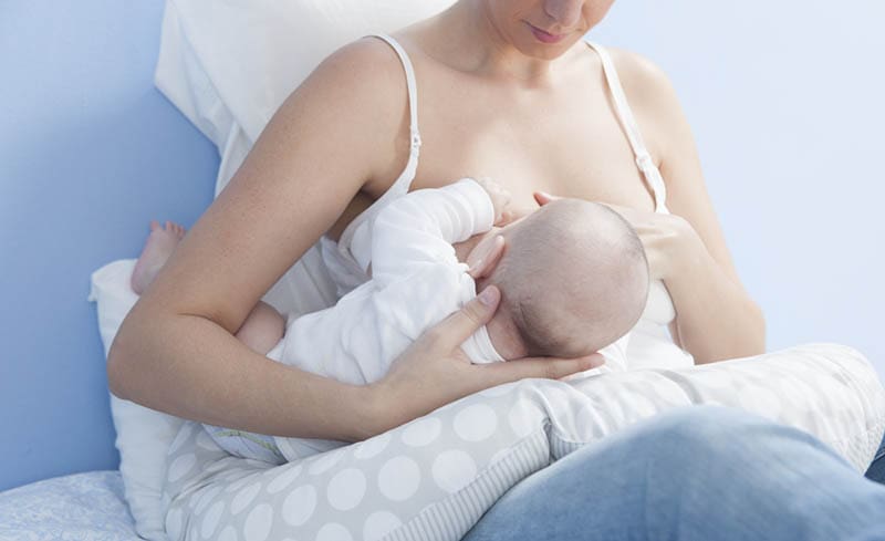 junge Frau, die Baby auf Schwangerschaftskissen stillt