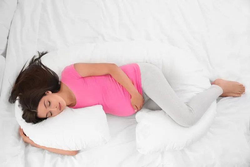 junge schwangere Frau, die auf dem Schwangerschaftskissen schläft