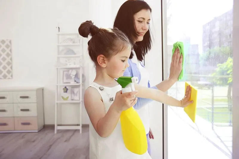 kleines Mädchen hilft Mutter, Fenster zu putzen