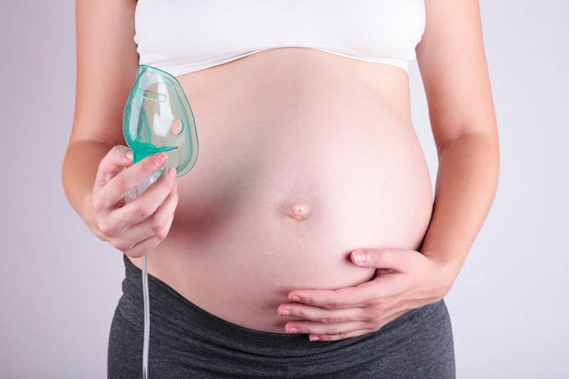 schwangere Frau, die Inhalationsmaske hält