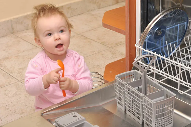 süßes Baby sitzt in der Nähe der Spülmaschine