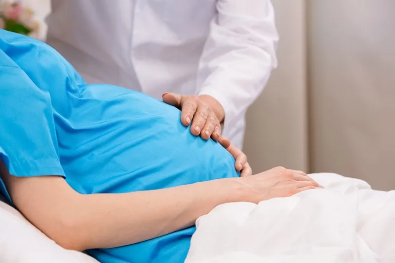 Arzt berührt schwangeren Frau Bauch auf dem Krankenhausbett
