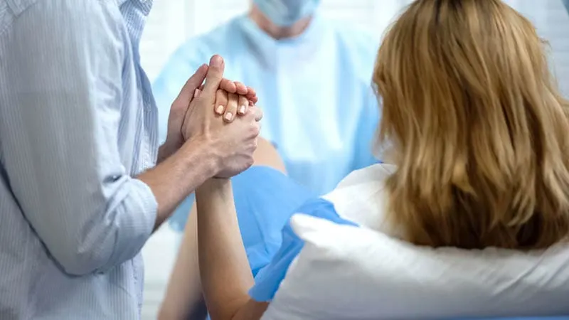 Arzt hält Frau für Hand, während sie gebiert