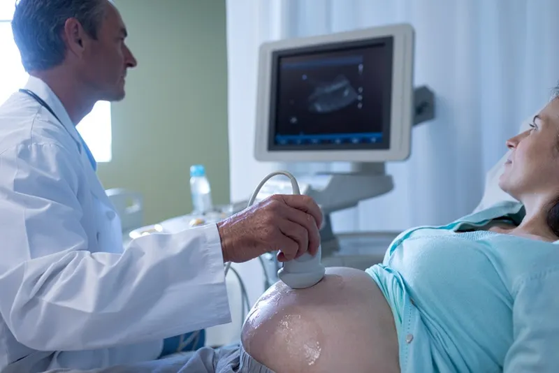 Arzt macht Ultraschalluntersuchung der schwangeren Frau im Krankenhausbüro