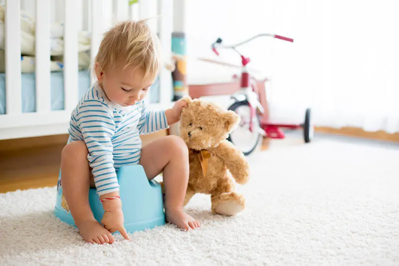 Baby, das auf einem Töpfchenzug sitzt, der ein Teddybärspielzeug hält