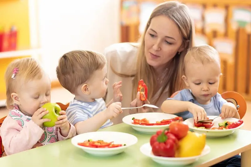 Babys essen gesunde Mahlzeit mit ihrem Lehrer im Kindergarten