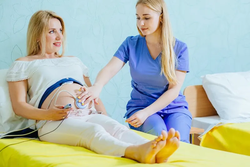 Blonder junger Hebammenuntersuchungsbauch der hübschen blonden schwangeren Frau mit CTG-Abtastung in der Praxis