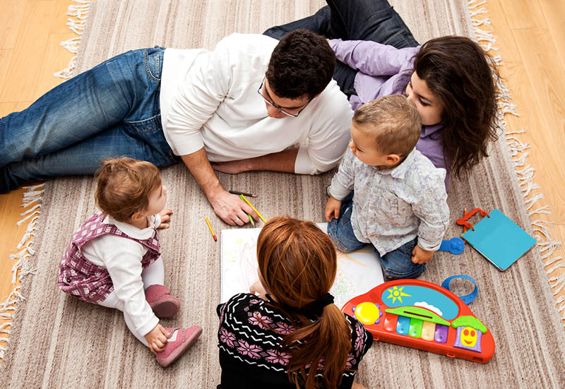 Eltern genießen mit drei Kindern auf dem Boden mit Kinderspielzeug