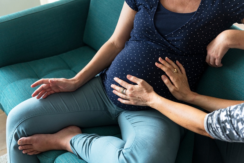Frau kuschelt den schwangeren Bauch ihrer Freundin auf der Couch