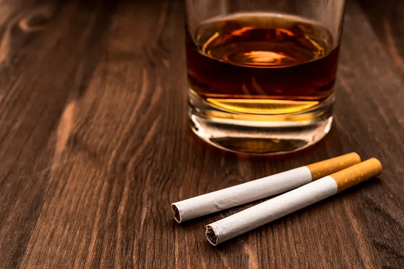 Glas Whisky und zwei Zigaretten neben Glas auf dem Holztisch