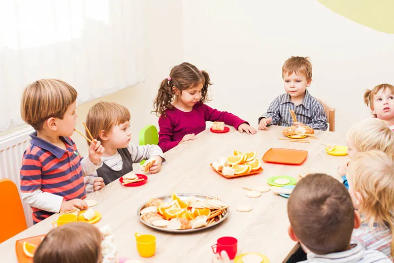Gruppe von Kindern, die am Tisch sitzen und eine Mahlzeit im Kindergarten essen