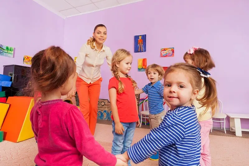 Gruppe von entzückenden Kindern, die mit ihrem Lehrer im Kindergarten spielen