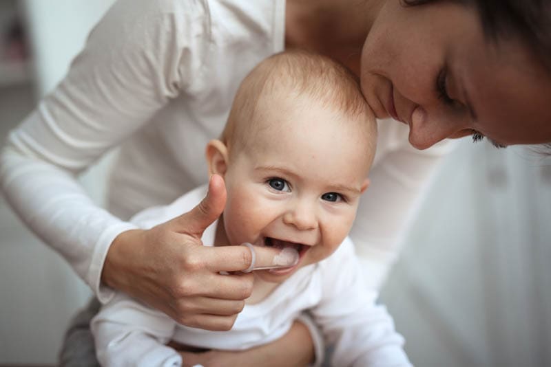 Mama hilft, die Zähne eines glücklichen Babys zu putzen