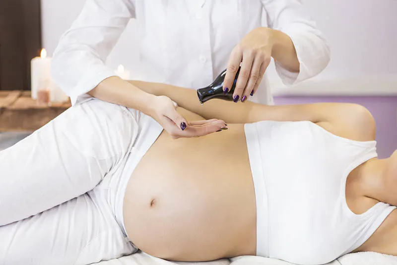 Massagetherapeut mit Aromaöl zum Massieren einer schwangeren Frau auf dem Schreibtisch