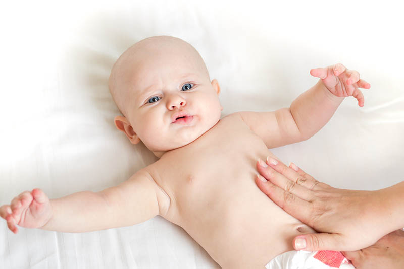 Mutter Hände massieren niedlichen Babybauch, während Baby Schluckauf hat