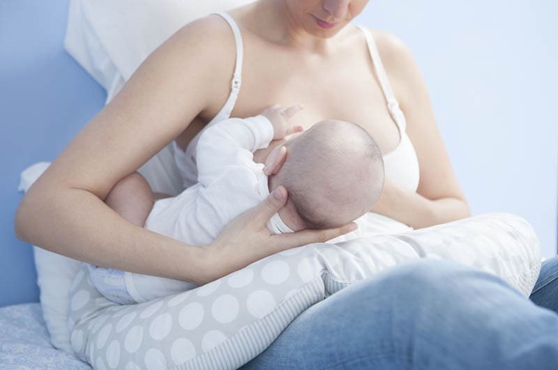 Mutter benutzt ein Stillkissen zum Stillen ihres Babys auf dem Bett