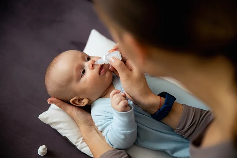 Mutter mit Nasentropfen für Baby laufende Nase