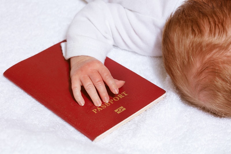 Reisepassdokument unter der Hand des kleinen Neugeborenen