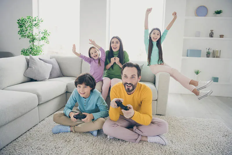 Vater und Sohn spielen Videospiele und Mutter und Töchter jubeln ihnen zu