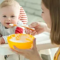 Mutter füttert ihr lächelndes Baby mit Brei