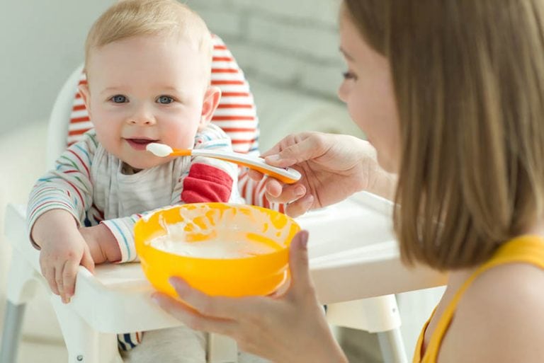 Mutter füttert ihr lächelndes Baby mit Brei