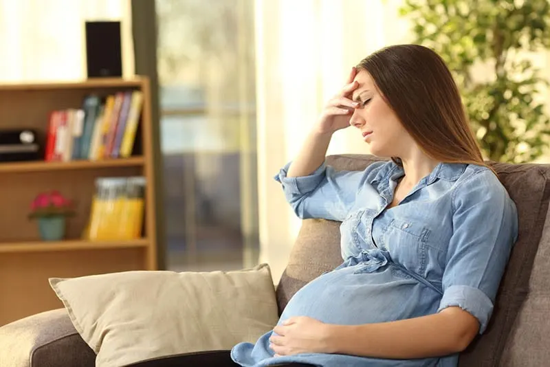 betonte schwangere Frau, die auf der Couch sitzt und Hand auf Stirn hält