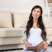 junge schwangere Frau, die eine schwangere Checkliste zu Hause schreibt