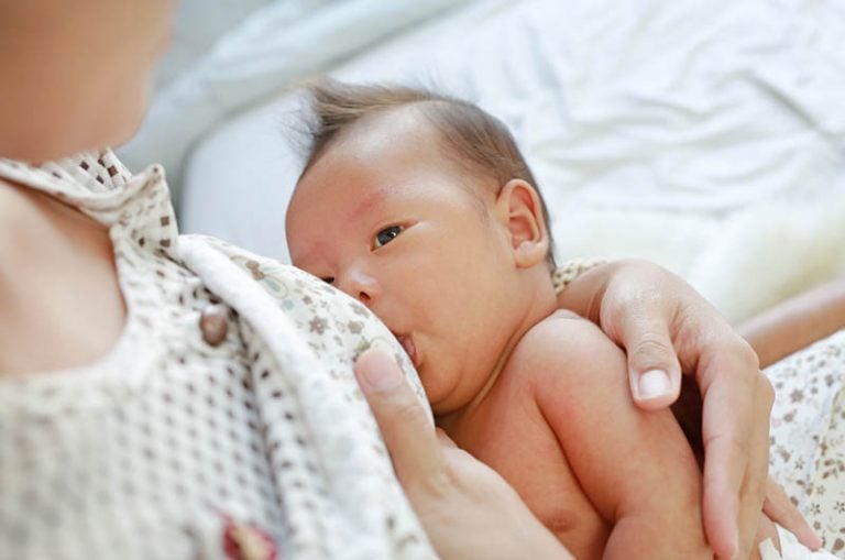 Mutter trägt Pyjama stillendes Baby auf dem Bett