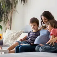 schwangere Frau, die ein Buch mit zwei Kindern liest