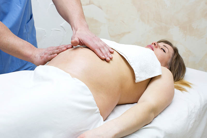 entspannte schwangere Frau, die auf einem Schreibtisch liegt und Massage hat