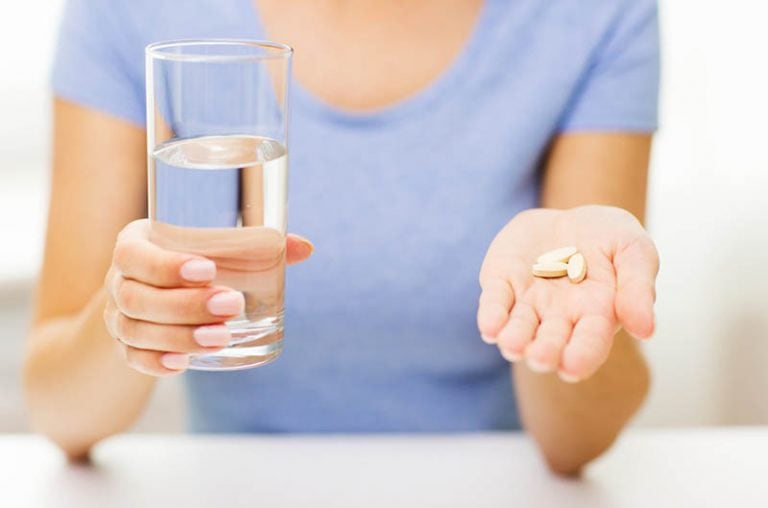 Frau, die blaues Hemd hält, das Pillen und Glas Wasser hält