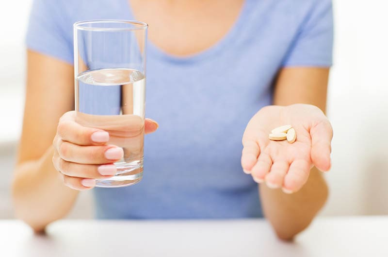 Frau, die blaues Hemd hält, das Pillen und Glas Wasser hält