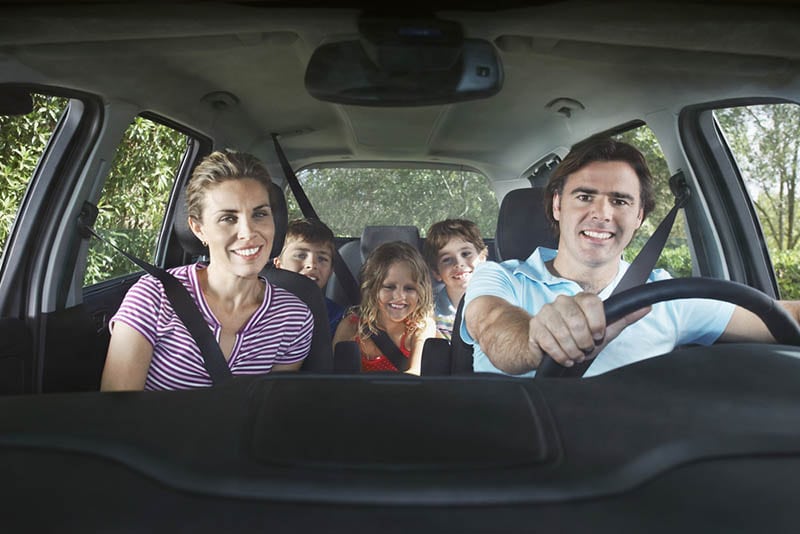 glückliche Eltern, die mit ihren drei Kindern im Auto fahren