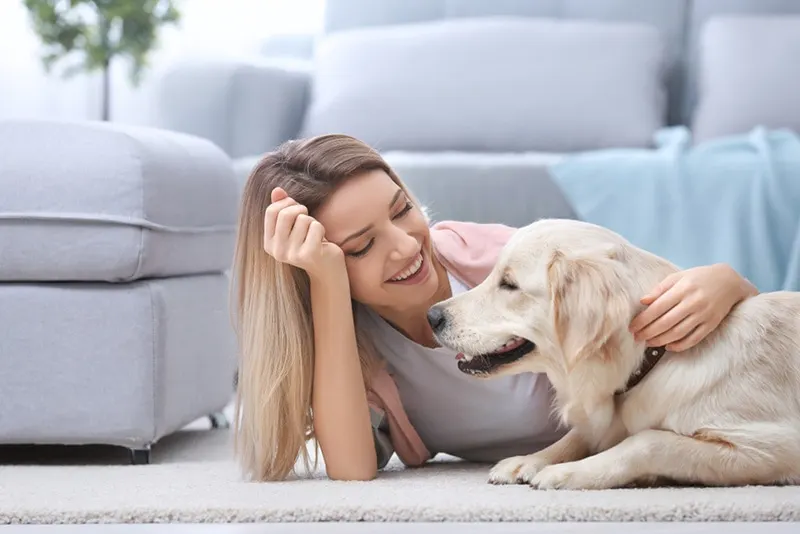 glückliche junge Frau, die ihren Hund zu Hause auf dem Boden kuschelt