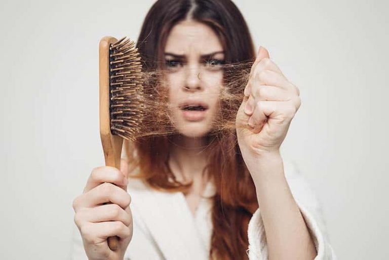 eine schockierte Frau mit einer Haarbürste und einigen gefallenen Haaren