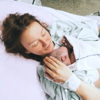 junge Frau hält ihr neugeborenes Baby direkt nach der Geburt im Krankenhaus