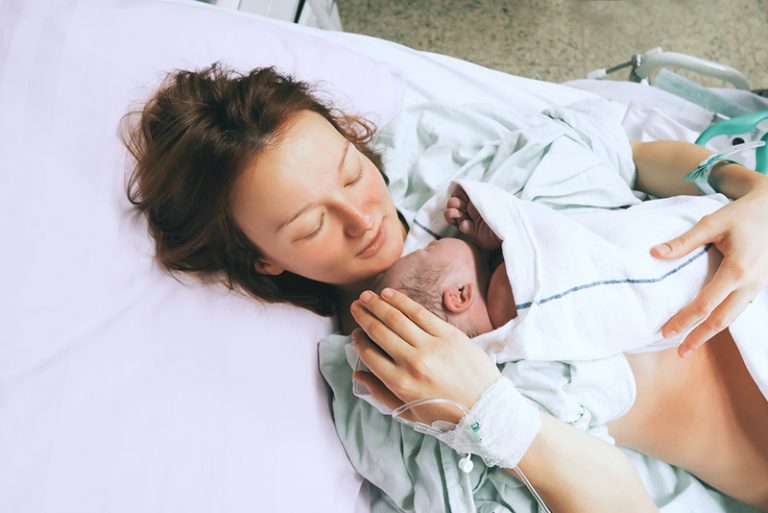junge Frau hält ihr neugeborenes Baby direkt nach der Geburt im Krankenhaus