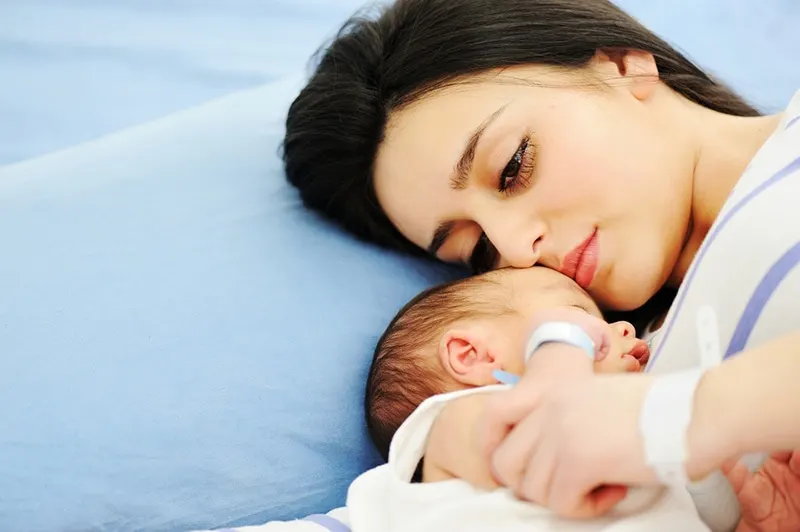 junge Frau mit Schmerzen auf dem Krankenhausbett mit ihrem Neugeborenen liegen