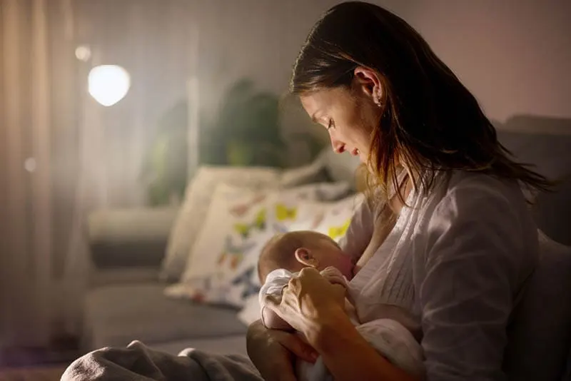 junge Mutter stillt ihr neugeborenes Baby nachts im Wohnzimmer