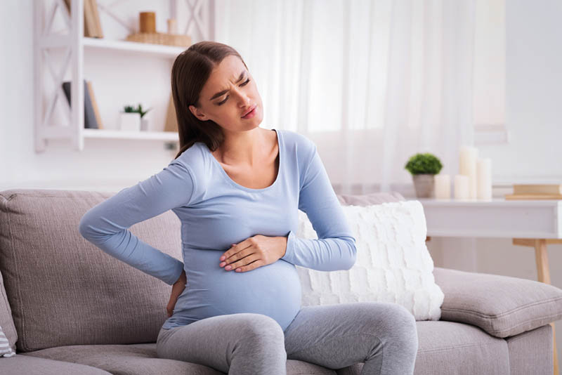 junge schwangere Frau, die auf der Couch sitzt und Bauchschmerzen fühlt