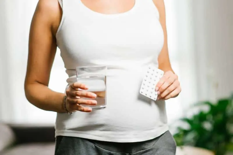 junge schwangere Frau, die eine Folsäurepille und ein Glas Wasser hält