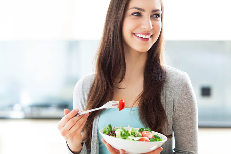 lächelnde junge Frau, die Entfernung betrachtet und einen Salat von der Schüssel isst